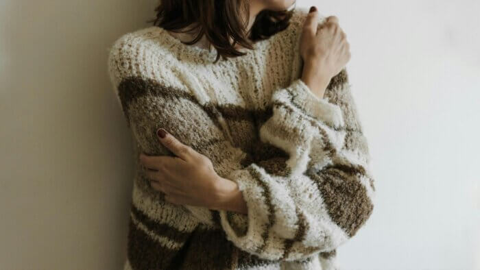 A woman wearing a plant wool jumper with arms crossed over her body